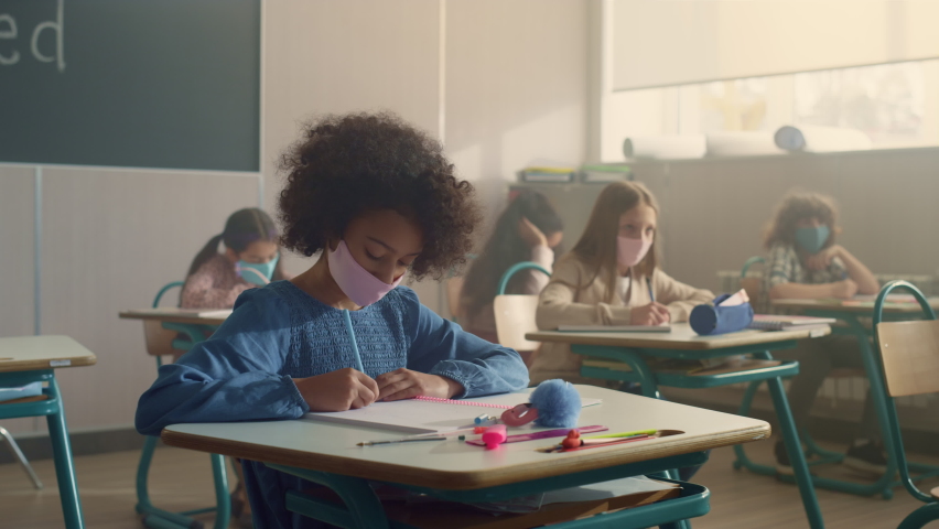 Mixed race children in medical masks studying at school desks during coronavirus pandemic. Diverse kids making notes in exercise books. Smart pupils in protective masks learning science in classroom  Royalty-Free Stock Footage #1074894260