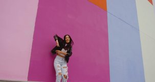 4K Beautiful , stylish , young girl with black hair  beautiful body in Leather Jacket and sport jeans  dancing , moving , smiling and looking at camera with happy emotions . Slow motion colorful wall
