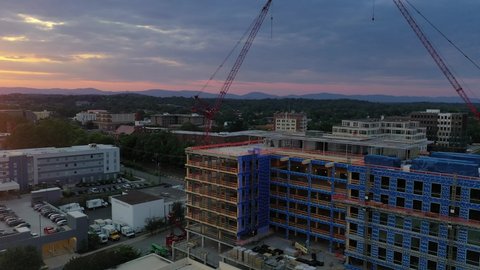 Raw aerial 4K sunset reveal footage of new under construction  residential apartment condo complex with partial siding, two red cranes in downtown Charlottesville Virginia dramatic colorful sky
