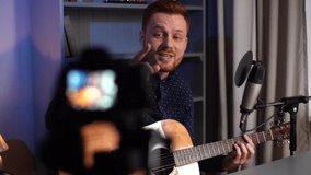 Tracking shot of happy guitarist singer male playing acoustic guitar and singing song, recording video with camera for online music vlog or followers at home studio. Shooting in slow motion.
