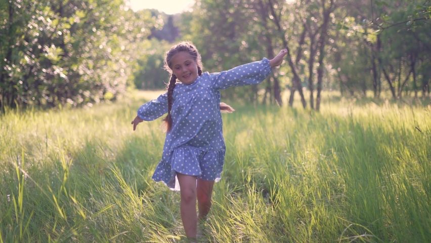 Happy girl. Little girl run through forest park. Kid plays on green grass. Happy kid run in garden. Green grass and trees in forest park. Little girl run through green garden.Happy girl among trees
