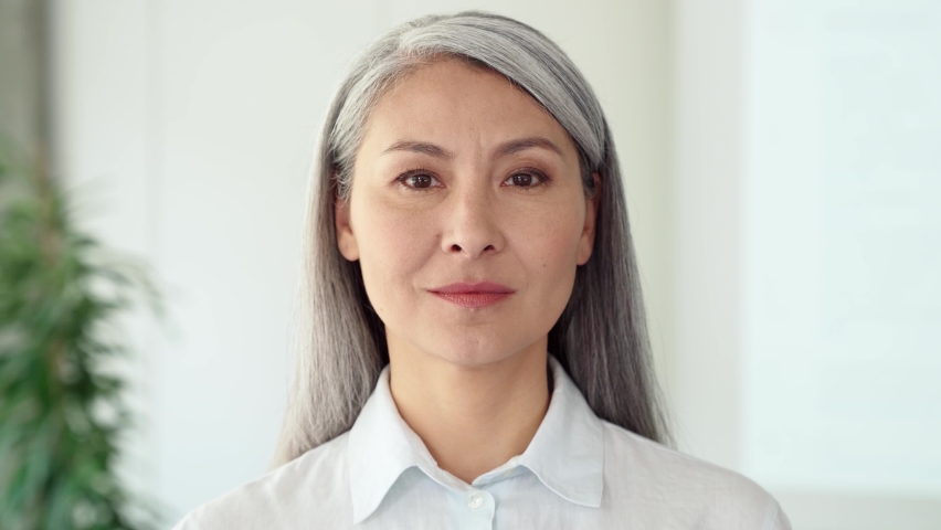 Confident serious ambitious middle aged adult Asian older senior female business woman corporation ceo in modern office posing looking at camera. Business career concept. Closeup portrait headshot. | Shutterstock HD Video #1074905678