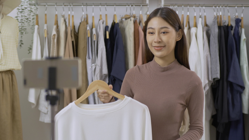 Young bautiful woman selling her clothing. She using smartphone to live streaming with customer.