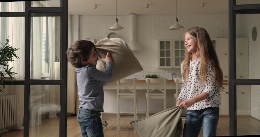 Crazy small child boy fighting pillows with laughing older sister in modern living room. Carefree little kids siblings best friends having fun entertaining playing cushion battle on weekend at home. Royalty-Free Stock Footage #1074914744
