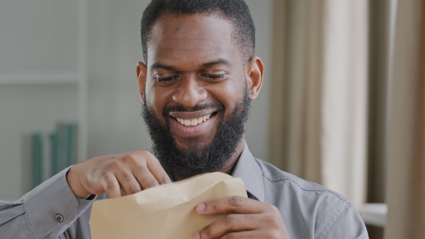 Excited black male executive receiving mail with salary growth payment, business loan approval. Happy overjoyed businessman opening envelope reading great news in paper letter sitting at workplace Royalty-Free Stock Footage #1074916928