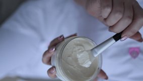 a white face mask is collected with a brush from a jar. the concept of care and youth. cosmetologist's office. Vertical Video