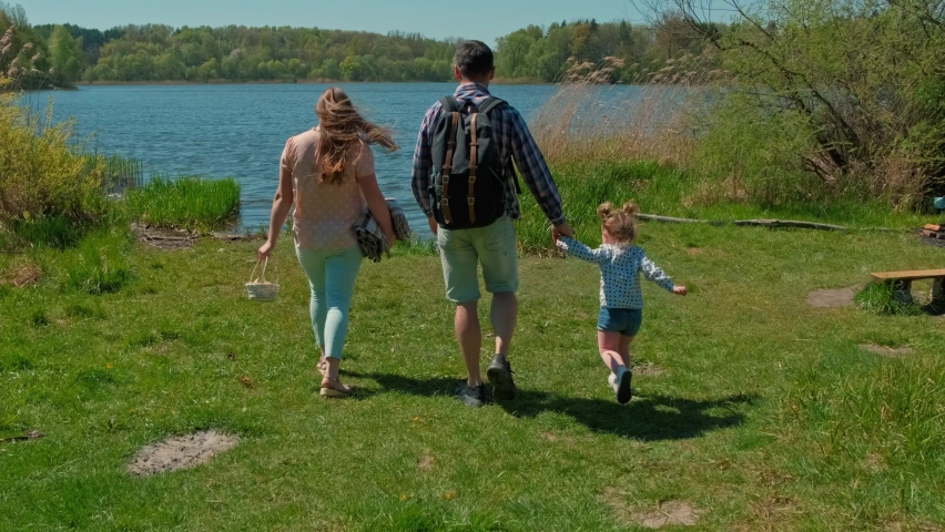 Happy cute family walking in nature park by lake. Parents with child walking. Family picnic by lake. Hiking in natural park Royalty-Free Stock Footage #1074923909