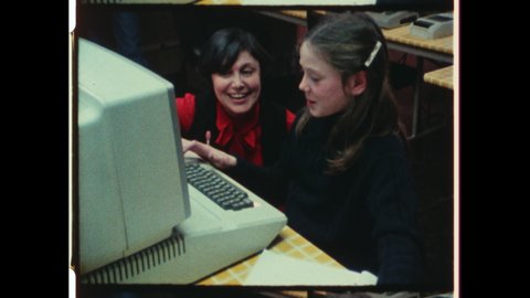 1980s Columbus, OH. An Elementary School Teacher helps student on Apple Macintosh Computer. The Student and teacher laugh while interacting. 4K Overscan of Vintage Archival 16mm Film Print
