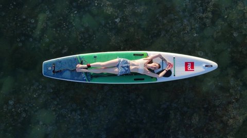 May 27, 2021. Anapa, Russia. Woman posing on stand up paddle board at blue sea. Relaxing on Red paddle sup board. Aerial view