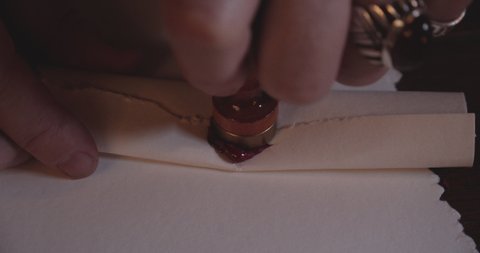 Closeup shot of a parchment paper with a circular red wax laid out on the edges, with a stamp to seal the parchment.