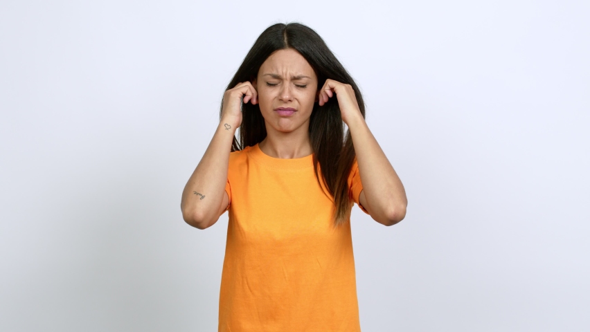 Young woman covering both ears with hands. Frustrated expression over isolated background