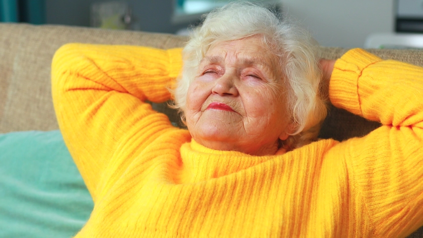 mature woman dreaming, thinking about good future sitting on sofa in living room