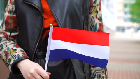Unrecognizable woman holding Holland flag. Girl walking down street with national flag of Netherlands