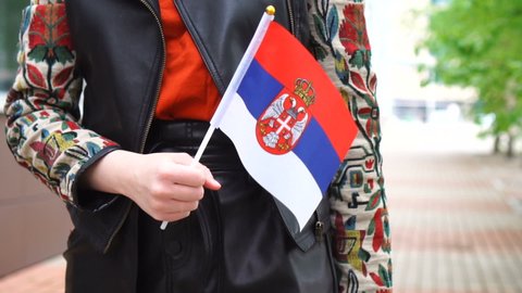 Unrecognizable woman holding Serbian flag. Girl walking down street with national flag of Serbia
