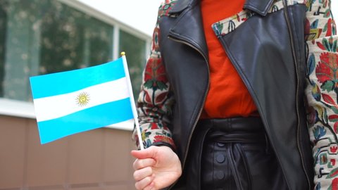 Unrecognizable woman holding Argentinian flag. Girl walking down street with national flag of Argentina
