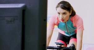 close up of sweaty asian woman wearing wearable smart watch riding exercise bike and watching online video sports lesson on television in living room at home