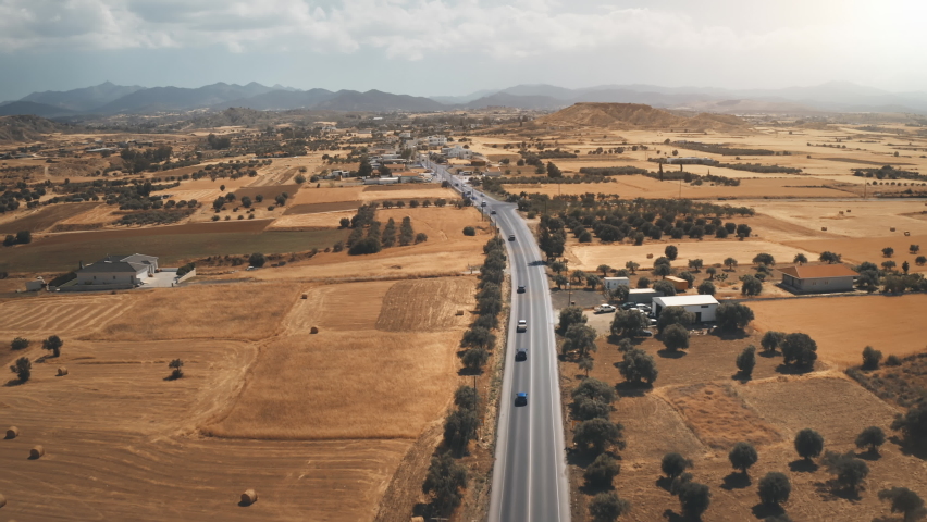Cars drives in desert road aerial. Yellow fields, gardens and mountain range. Summer travel to Cyprus. Autumn countryside. Beautiful landscape. Tourism, vacation, holiday, journey. Cinema drone flight
