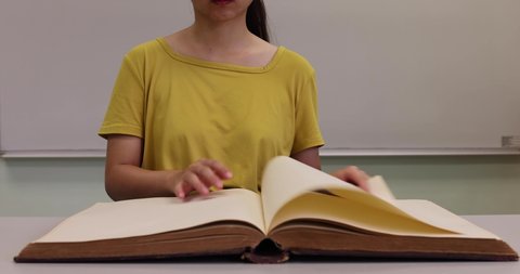 young lady turns pages of an old and big book (selective focus on girl)