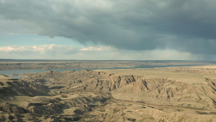 Clouded Sky Over Vast Erosion Cliffs With Agricultural Farmland near Lake Diefenbaker, - Aerial Drone Shot