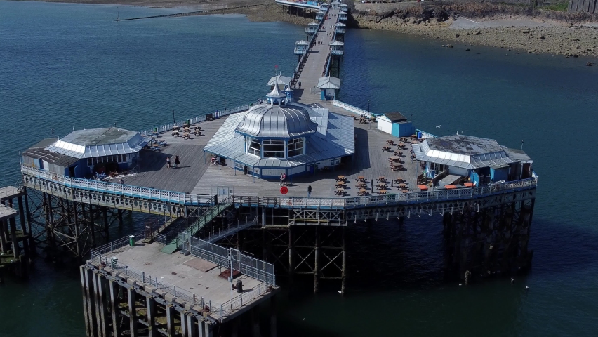 Llandudno pier seaside resort landmark silver pavilion wooden boardwalk aerial view orbit left slowly