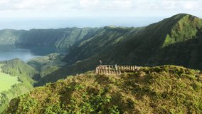 Aerial shot of male hiker sitting at Miradouro do Cerrado das Freiras viewpoint, Sao Miguel island, Azores, Portugal, Europe. Young man overlooking mountain landscape of island with lakes, 4k footage