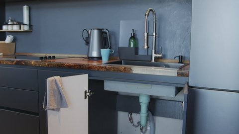 Tilt up slowmo shot of disassembled pipes and other plumbing parts lying on floor before kitchen sink with open cabinet