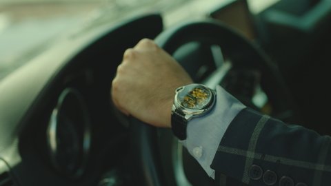 Close-up  hand of man driver sitting inside car interior and holding the rudder . Businessman in suit wearing expensive watch driving car . Driver hitting rudder 
