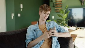 Caucasian male relaxing on couch texting on cellular device in home