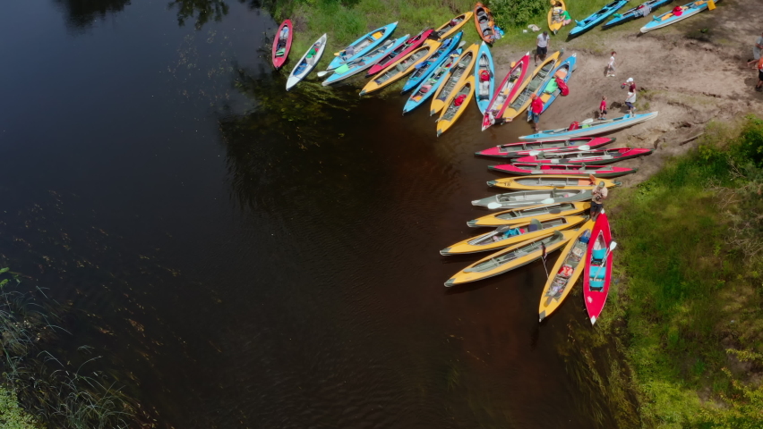 Camping river tourists with many colorful kayaks on the river bank. River tourism - people and families spend weekends on a river kayaking trip. Aerial drone shot.