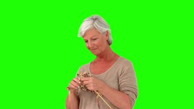 Retired woman knitting against a green screen