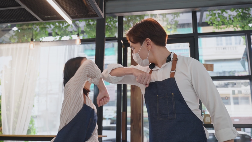 Asian waiter worker greeting waitress girl by elbow bump in restaurant. Attractive cafe businessman owner wear protective mask due to Covid19, feel happy and confidence for new normal in coffee shop. Royalty-Free Stock Footage #1074962291