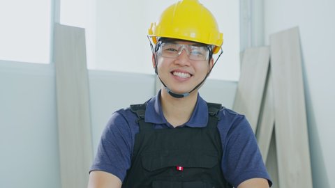 Portrait of Asian Craftsman or Carpenter builder man look at camera. Young Construction worker or Joiner male wear protective eyeglasses and helmet at workplace for safety while work to renovate house