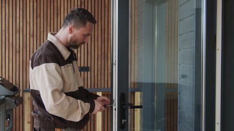 Slowmo medium shot of handyman in uniform using screwdriver and repairing door lock