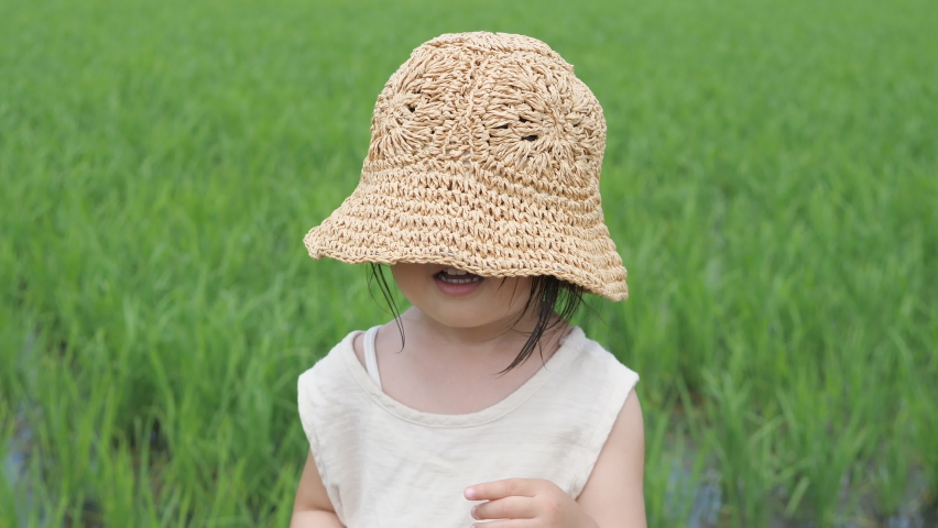 Happy smiling Asian little girl in straw hat. Paddy field planted with rice seedlings in the background. Early summer. Preschool toddler infant child. Safe and healthy food ingredients agriculture