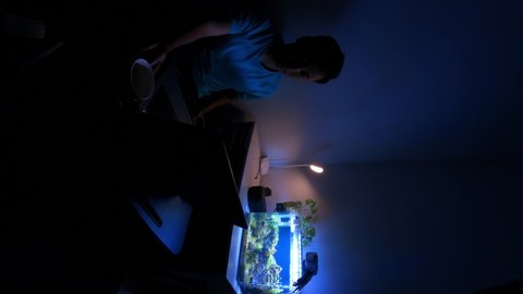 Timelapse of a young man working with a laptop in the darkroom with aquascape aquarium, coffee, and warm light desk lamp. Footage with Vertical Screen Orientation 9:16