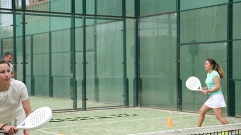 Sportive woman playing padel. In the background, athletes are training. High quality 4k footage