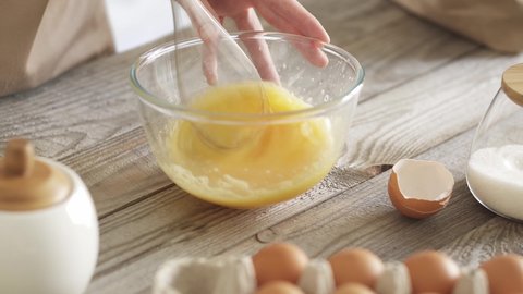 Beating chicken eggs to prepare the dough. Mixing chicken egg yolks in a transparent glass bowl Tray of eggs, eggshells and sugar bowl in the foreground. Beat chicken eggs with a blender whisk
