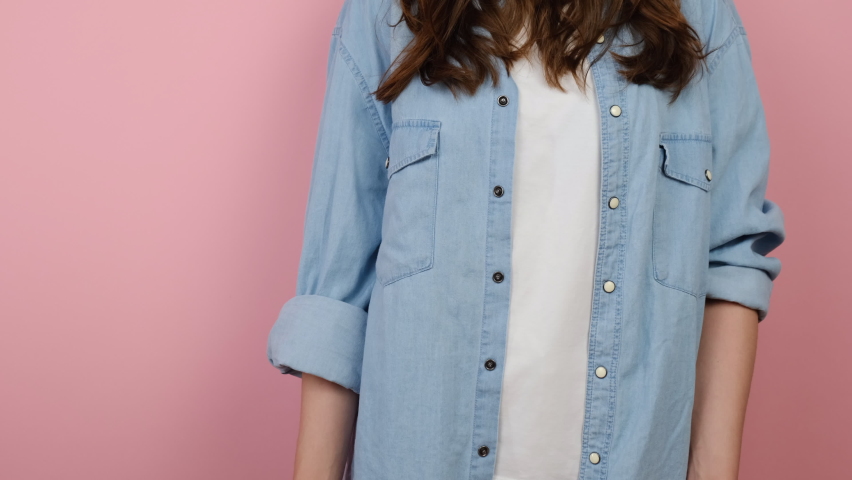 Close up cropped young woman holds yellow arrow pointing on palm with copy space for promotional content, wears blue shirt, posing isolated on pink background in studio. Advertising area mock up