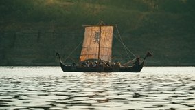 Vikings Sail on an Old Ship with a Lowered Sail on a Calmt River Against the Backdrop of Rocky Mountains. Concept on the theme of the Vikings and the early Middle Ages. - Powered by Shutterstock - Get 15% off with code: PIKWIZARD15