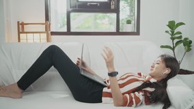 Asian woman relaxing on sofa at home with laptop browsing internet for home Female businesswoman talking a video call Conference or chat distancedistance learning while being self-isolated in quarant
