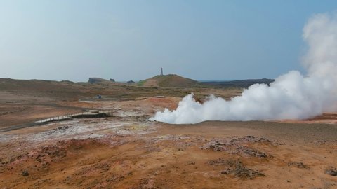ICELAND - CIRCA 2020s - Aerial past steaming hot fumeroles in a geothermal aera reveals the pretty Reykjanes lighthouse in the distance.