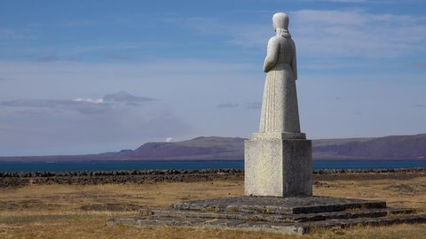 ICELAND - CIRCA 2020s - A statue overlooks a distant cloud of smoke from an erutping volcano, Iceland.