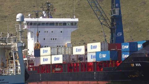 ICELAND - CIRCA 2020s - Cargo ships load containers full of fish at the fishing port of Vestmannaeyjar in the Westman Islands, Iceland.