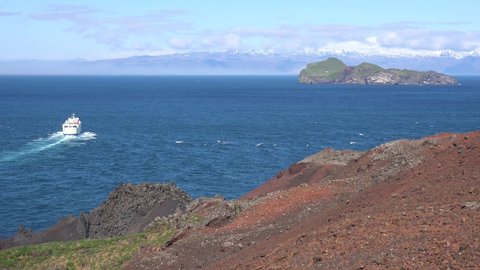 ICELAND - CIRCA 2020s - The Westman Islands all electric powered ferry boat leaves the harbor at Vestmannaeyjar passing high rising island cliffs.