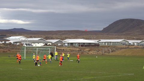 ICELAND - CIRCA 2020s - The Fagradalsfjall volcano is seen erupting in the distance behind a girls soccer match the town of Grindavik, iceland.
