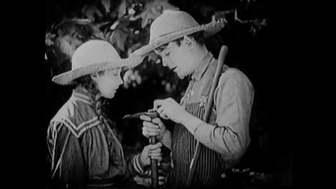 CIRCA 1919 - In this silent film, a young farmer flirts with a girl using his pickaxe.