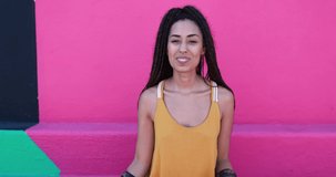 Young mixed race woman showing muscle biceps outdoor with pink background