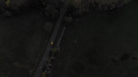 Drone flies over a small road at dusk as cars drive down a two-lane highway. cars, field and trees in a Aerial dark moody shot of road. car driving down a dark rural road outside the city at night.
