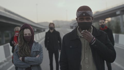 Handheld slowmo shot of group of young male and female protesters in face masks standing on highway outdoors and looking at camera