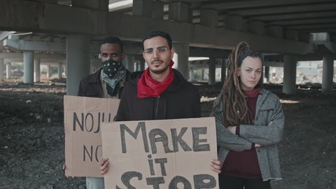 Slowmo portrait with dolly-out of young men with signs and woman standing under highway bridge and protesting before camera
